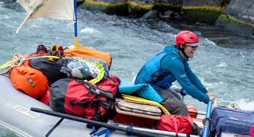 a person smiles as they captain a raft through whitewater 